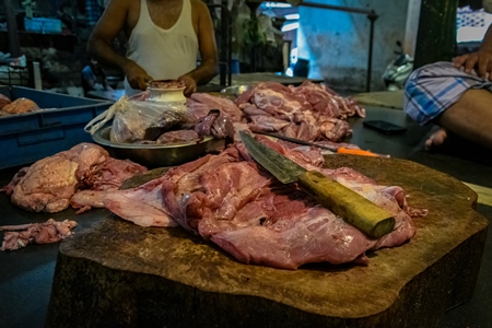 Buffalo meat being cut up by butchers on a chopping block at a meat market inside New Market, Kolkata, India, 2022