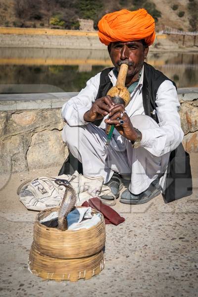 Snake charmer with orange turban outside Amber Fort playing pungi with snake in basket