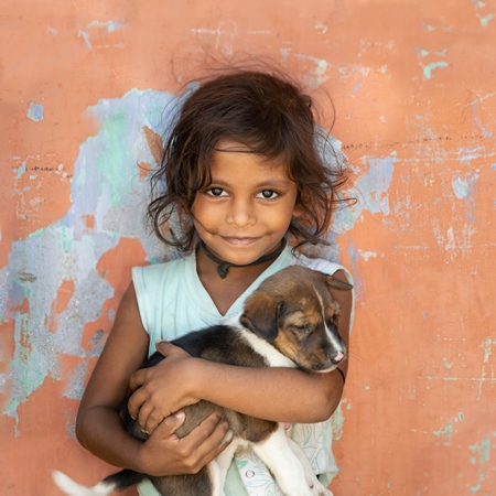 Girl with cute stray street puppy with orange wall background in village in rural Bihar