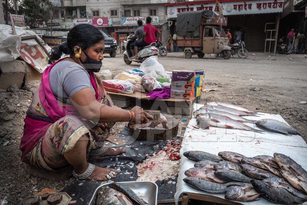 Roadside Indian fish stall or market with woman descaling fish in Pune, India, 2021