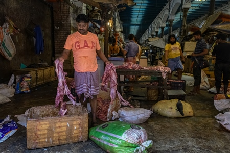 Worker handling pieces of meat at the meat market inside New Market, Kolkata, Inida, 2022