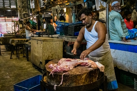 Buffalo meat being cut up by butchers at a meat market inside New Market, Kolkata, India, 2022