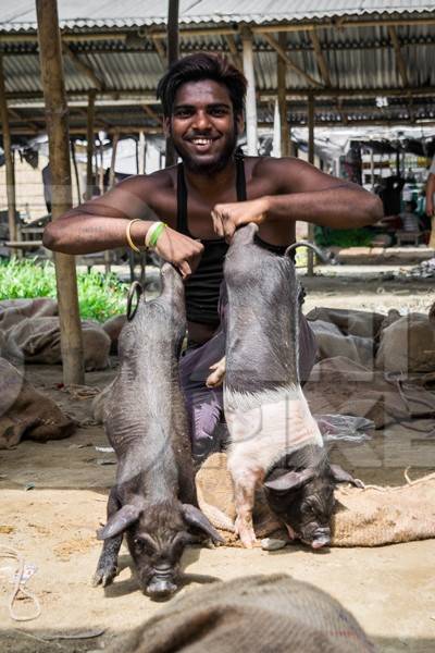 People holding pigs for sale for meat at the weekly animal market