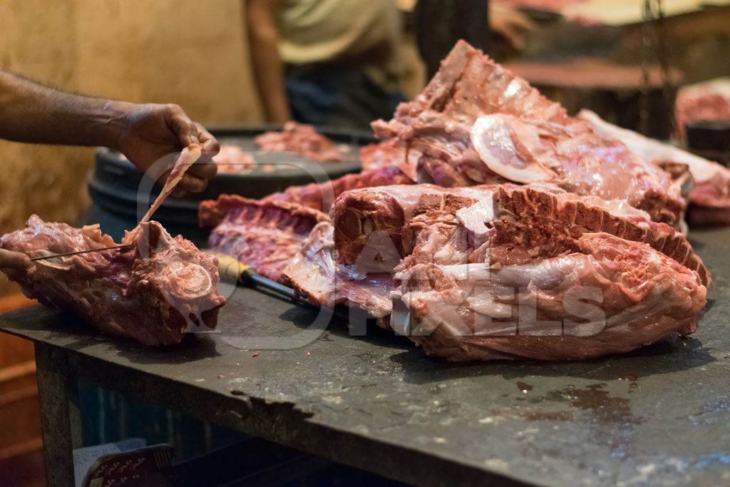Butcher cutting up piece of buffalo meat on block with knife in Crawford meat market in Mumbai, 2016
