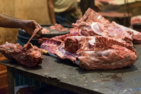 Butcher cutting up piece of meat on block with knife in Crawford meat market in Mumbai