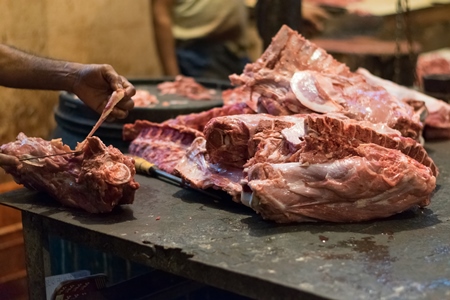 Butcher cutting up piece of buffalo meat on block with knife in Crawford meat market in Mumbai, 2016