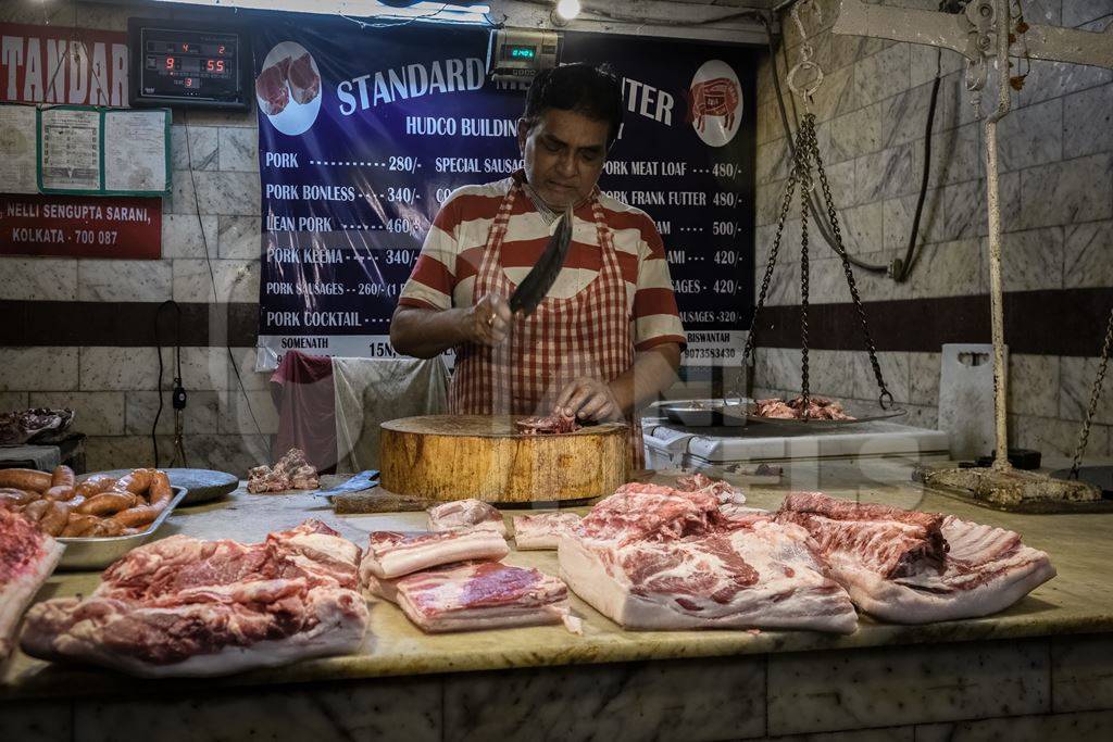 Worker or butcher cutting up parts of pig meat inside New Market, Kolkata, India, 2022