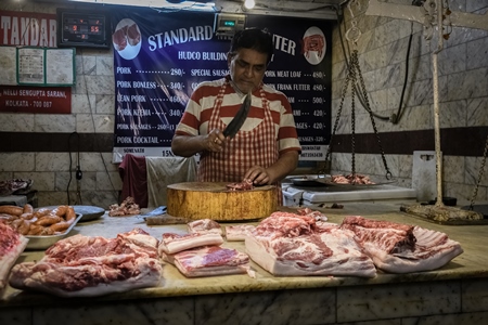 Worker or butcher cutting up parts of pig meat inside New Market, Kolkata, India, 2022