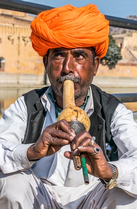 Snake charmer with orange turban outside Amber Fort playing pungi with snake in basket