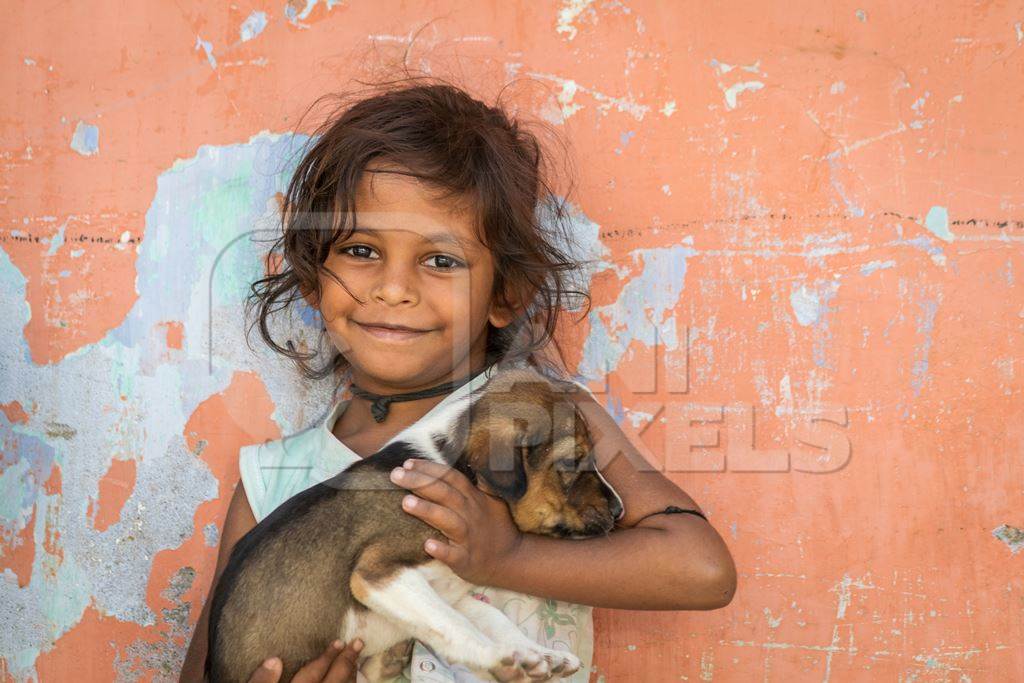 Girl with cute stray street puppy with orange wall background in village in rural Bihar
