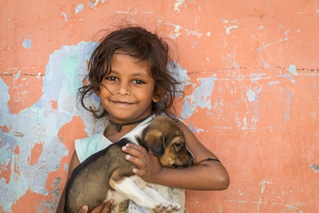 Girl with cute stray street puppy with orange wall background in village in rural Bihar