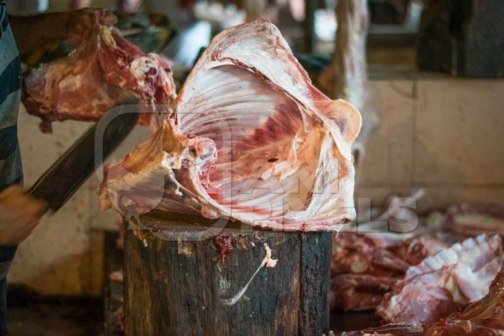 Butcher cutting up piece of meat on block with knife in Crawford meat market in Mumbai