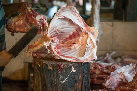 Butcher cutting up piece of meat on block with knife in Crawford meat market in Mumbai