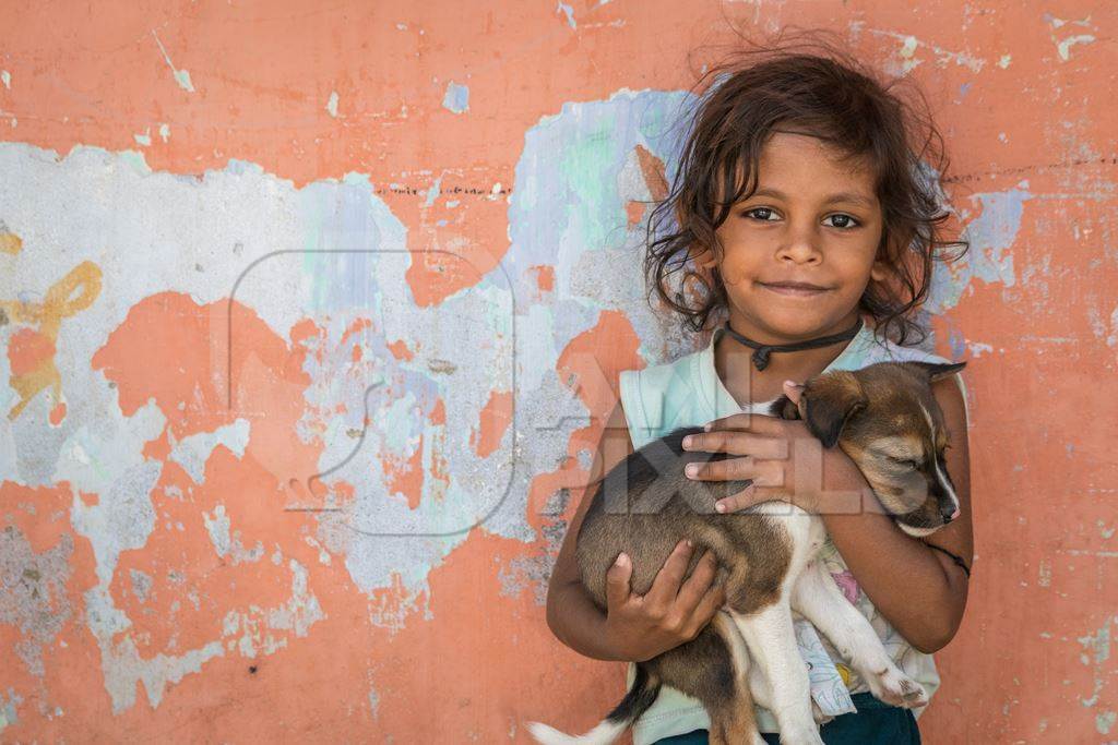 Girl with cute stray street puppy with orange wall background in village in rural Bihar