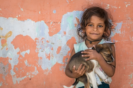 Girl with cute stray street puppy with orange wall background in village in rural Bihar