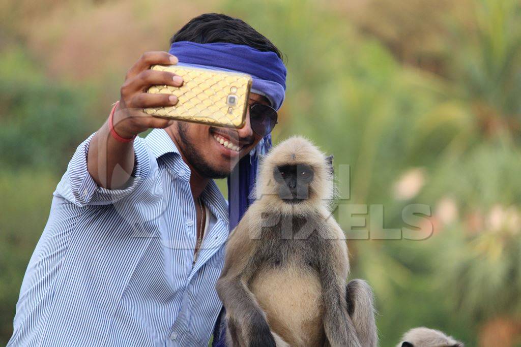 Man taking a selfie photo with a langur on mobile phone