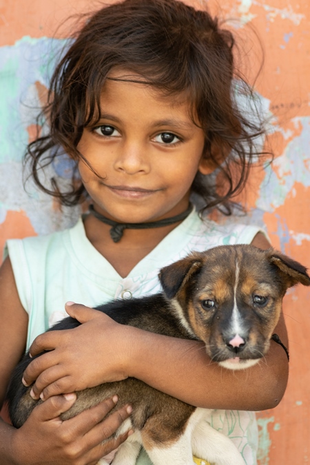 Girl with cute stray street puppy with orange wall background in village in rural Bihar