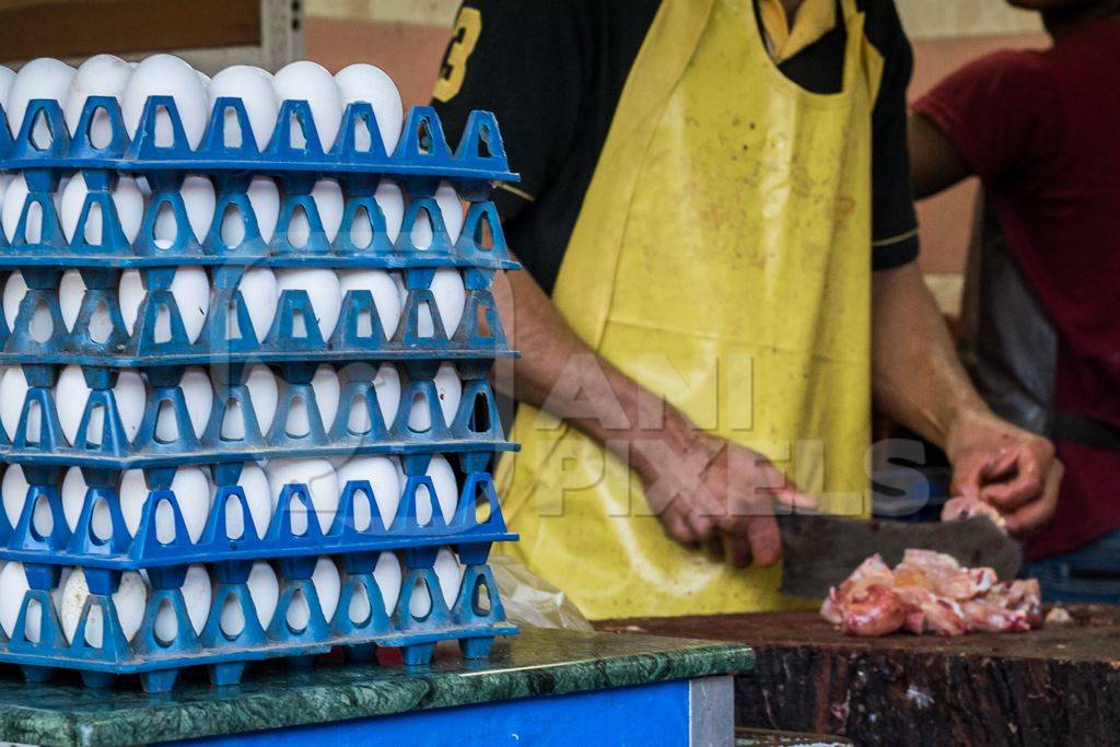 Butcher chopping up chicken with knife at a chicken shop with stack of eggs
