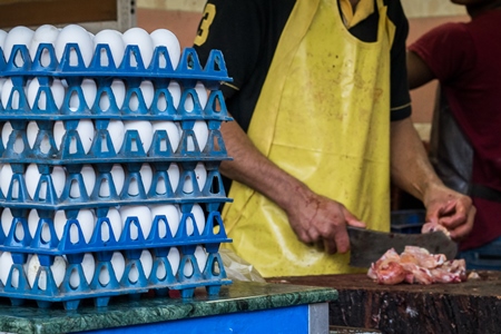 Butcher chopping up chicken with knife at a chicken shop with stack of eggs