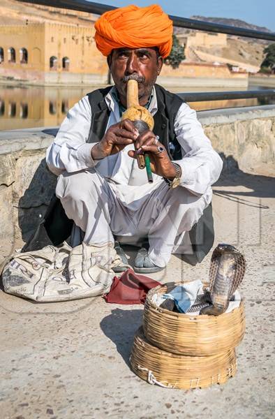 Snake charmer with orange turban outside Amber Fort playing pungi with snake in basket