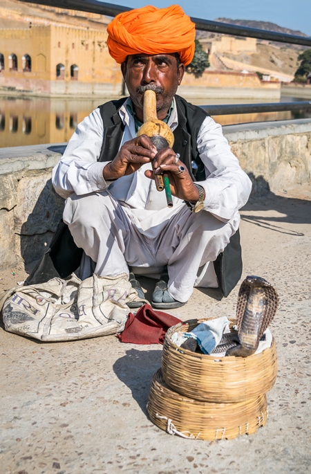 Snake charmer with orange turban outside Amber Fort playing pungi with snake in basket