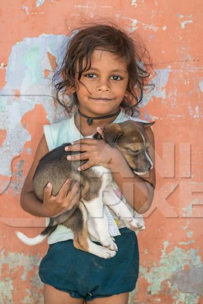 Girl with cute stray street puppy with orange wall background in village in rural Bihar