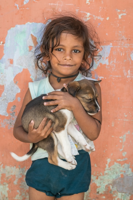 Girl with cute stray street puppy with orange wall background in village in rural Bihar