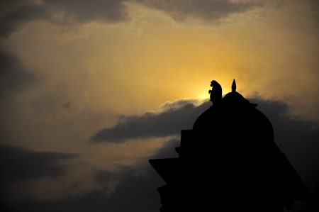 Silhouette of monkey sitting on top of temple at dawn or dusk