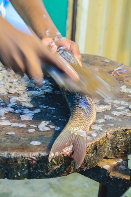 Man removing scales from a dead fish at a fish stall