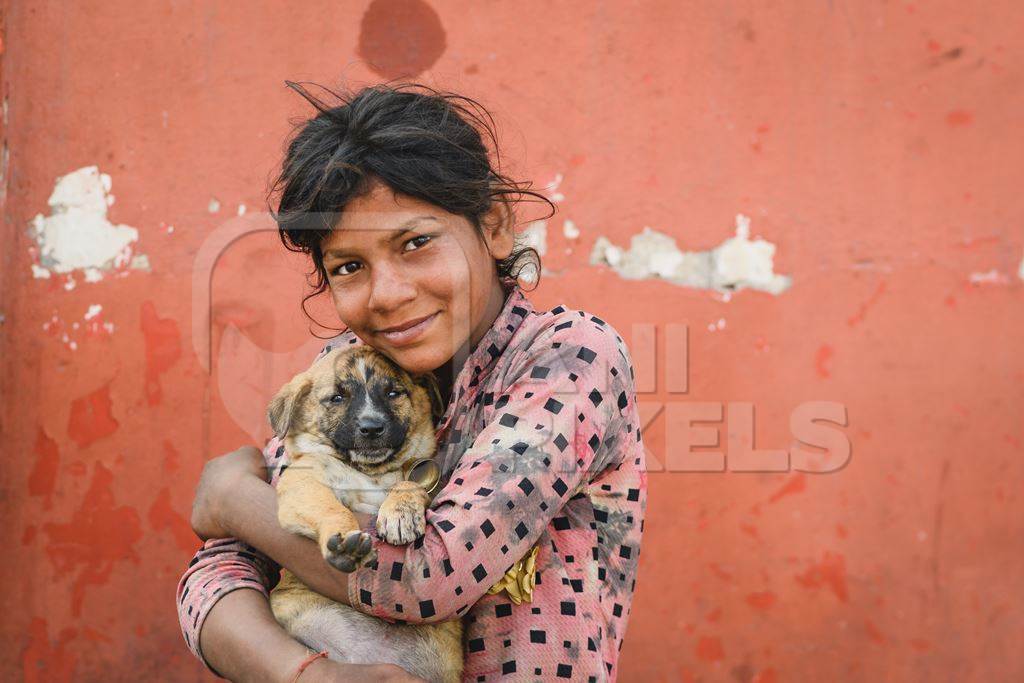 Portrait of girl holding Indian street or stray puppy dog with orange wall background, Jaipur, India, 2022