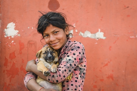 Portrait of girl holding Indian street or stray puppy dog with orange wall background, Jaipur, India, 2022