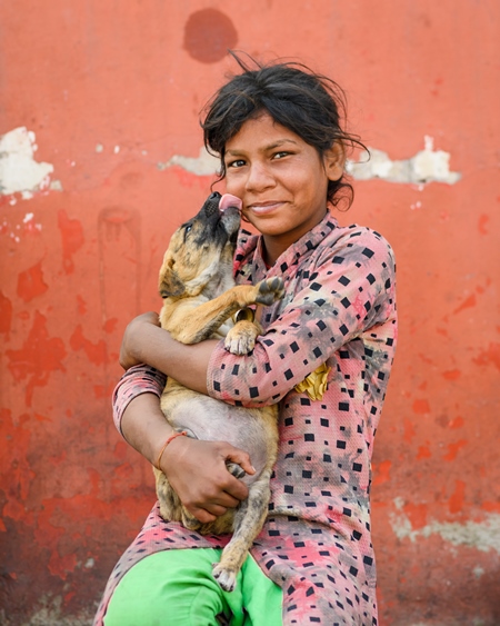 Portrait of girl holding Indian street or stray puppy dog with orange wall background, Jaipur, India, 2022